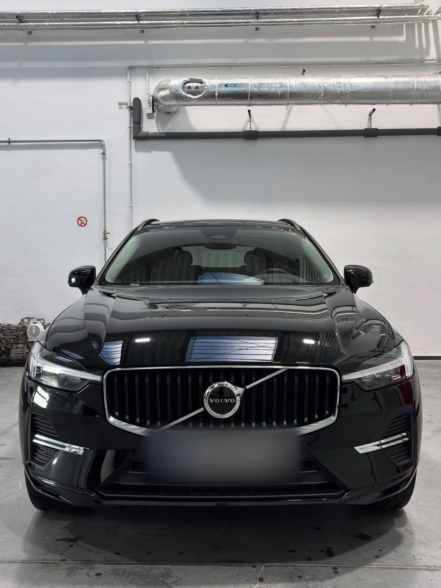 Czarne Volvo XC60 od frontu, w lakierze odbijają się lampy hali