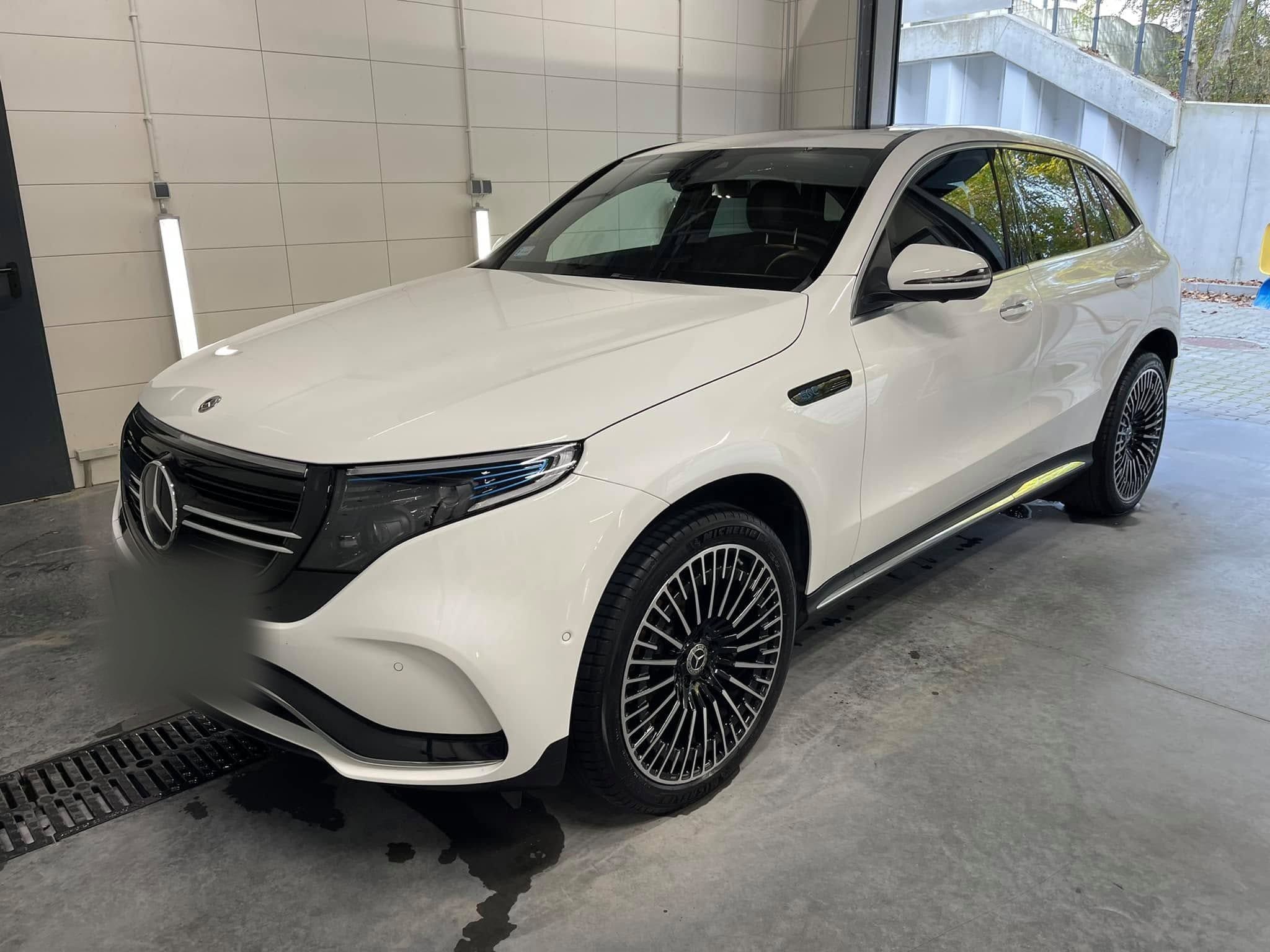 Biały Mercedes EQC na mokrej posadzce hali, w tle otwarta brama