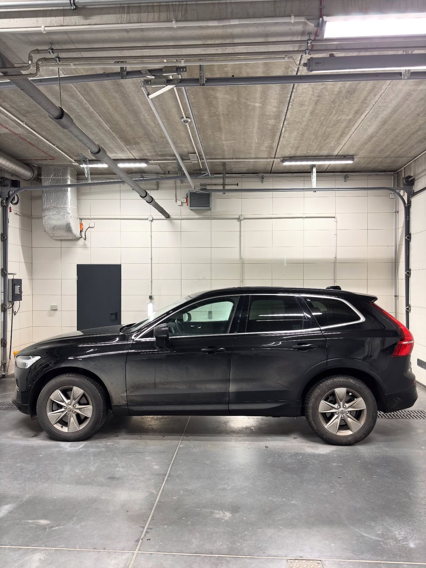 Hala GO+ Car Spa: czarne Volvo XC60 bokiem, białe ściany z płyt, bramy segmentowe i oświetlenie pod sufitem
